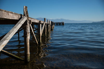 Wooden posts in sea against clear blue sky