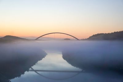 Scenic view of lake and bridge against sky during sunset