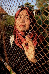 Portrait of young woman standing by chainlink fence