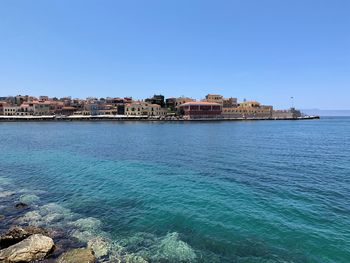 Scenic view of sea by buildings against clear blue sky