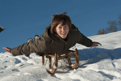 Portrait of happy man with sled on snow covered land against sky