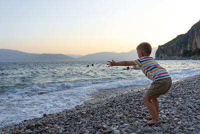 Boy on beach against sky during sunset