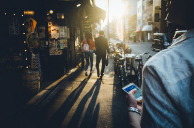 Midsection of woman using mobile phone on street in city