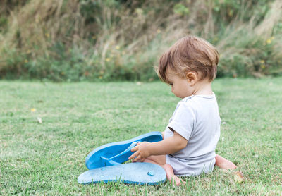 Toddler girl holding slippers while sitting on grassy field