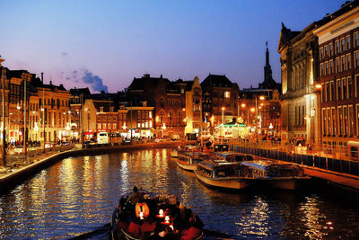 Boats on canal in illuminated city at dusk