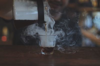 Midsection of barista pouring hot coffee in glass on table