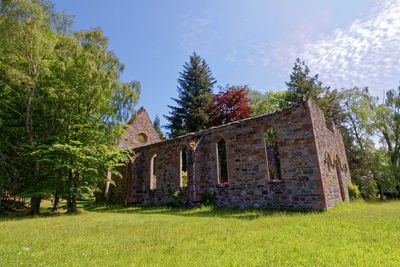 House amidst trees and plants on field against sky