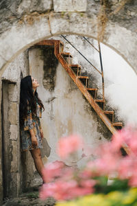 Side view of young woman standing against abandoned building