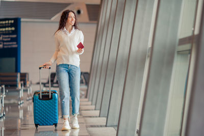 Full length of woman with luggage walking at airport