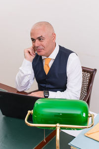 Young man using mobile phone while sitting on chair against wall