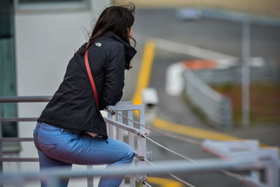 Rear view of woman standing on railing against blurred background