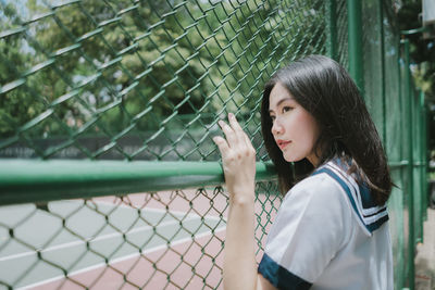 Side view of woman standing by chainlink fence