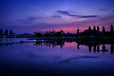 Reflection of silhouette buildings in lake against sky at sunset