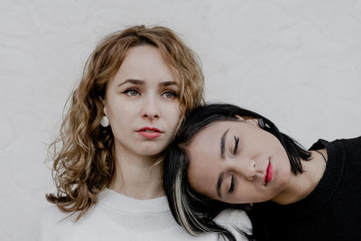 Woman leaning on thoughtful girlfriend looking away while sitting against wall