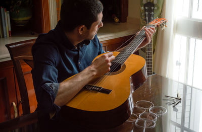 Man adjusting strings in guitar on table at home