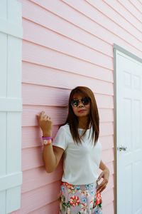 Young woman wearing sunglasses standing against wall