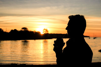 Silhouette man by lake against sky during sunset