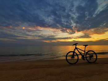 Bicycle on beach against sky during sunset