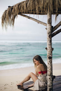 Woman sitting on beach by sea against sky