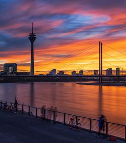 Bridge over river by buildings against sky during sunset