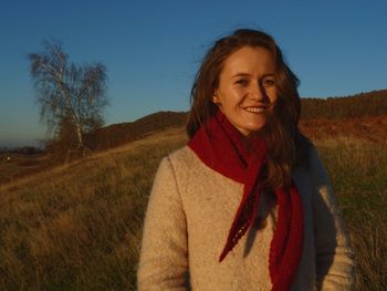 Portrait of smiling beautiful woman standing on grassy field against sky during sunset