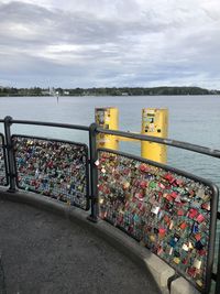 Padlocks on railing by river against sky