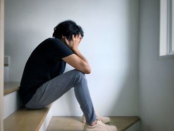 Side view of young man sitting on hardwood floor at home