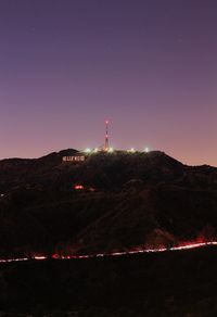 Lighthouse by mountain against clear sky at night