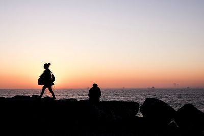 Silhouette people on beach against clear sky during sunset