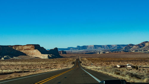 Road passing through landscape against clear blue sky