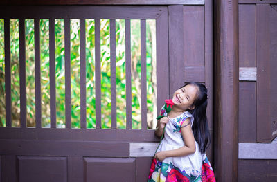 Portrait of smiling girl with flower standing against door
