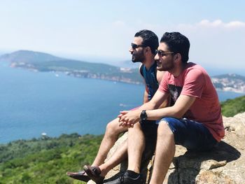 Friends sitting on rock against sky