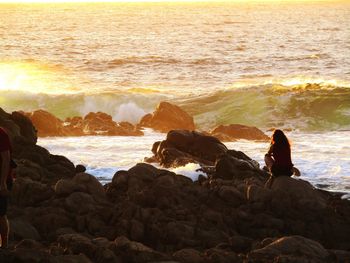 People on rock by sea against sky