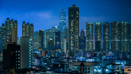 Illuminated modern buildings in city against sky at night