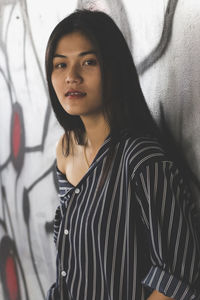 Portrait of beautiful young woman leaning on graffiti wall