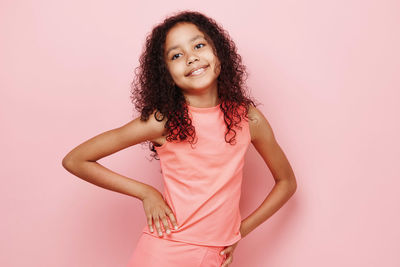 Portrait of young woman standing against pink background