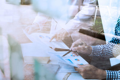 Midsection of businesswomen discussing over graph seen through glass window