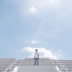 Low angle view of young man standing on steps against sky