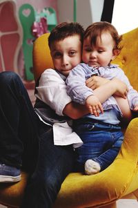 Cute siblings sitting on chair at home