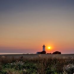 Lighthouse by sea against sky during sunset