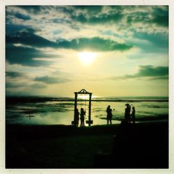 Silhouette people on beach against sky during sunset