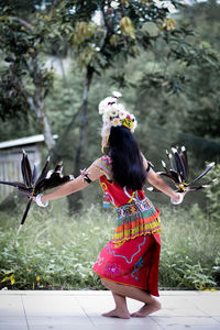 Side view of young woman with arms raised standing against trees