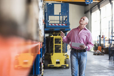 Man with tablet walking in industrial hall looking at shelves