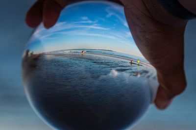 Close-up of person hand holding crystal ball against sea and sky