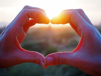 Close-up of hands making heart shape against sky during sunset