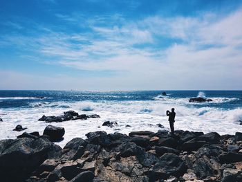 People standing on rock by sea against sky