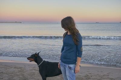 Woman with dog at beach during sunset