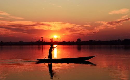 Silhouette man on boat in lake against sky during sunset