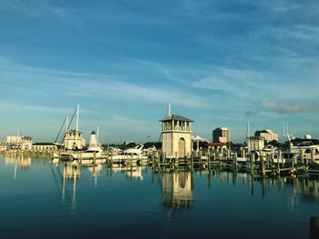 Sailboats moored in harbor by buildings against sky