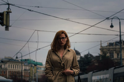 Portrait of young woman standing against sky in city